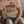 Load image into Gallery viewer, A man sitting on a wooden dock by a lake wearing a beige graphic t-shirt with a retro sunset design and the text 'GO UP NORTH'.

